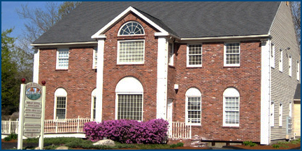 The image shows a two-story brick house with white trim, a front porch, and a red roof. There is a sign on the lawn that reads THE HILL HOSPITAL.